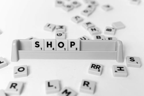 Free Scrabble tiles spelling 'Shop' on a rack surrounded by scattered tiles on a white surface. Stock Photo