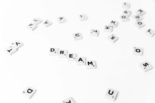 Free Scrabble tiles spelling 'dream' on a scattered white background, conceptual image. Stock Photo