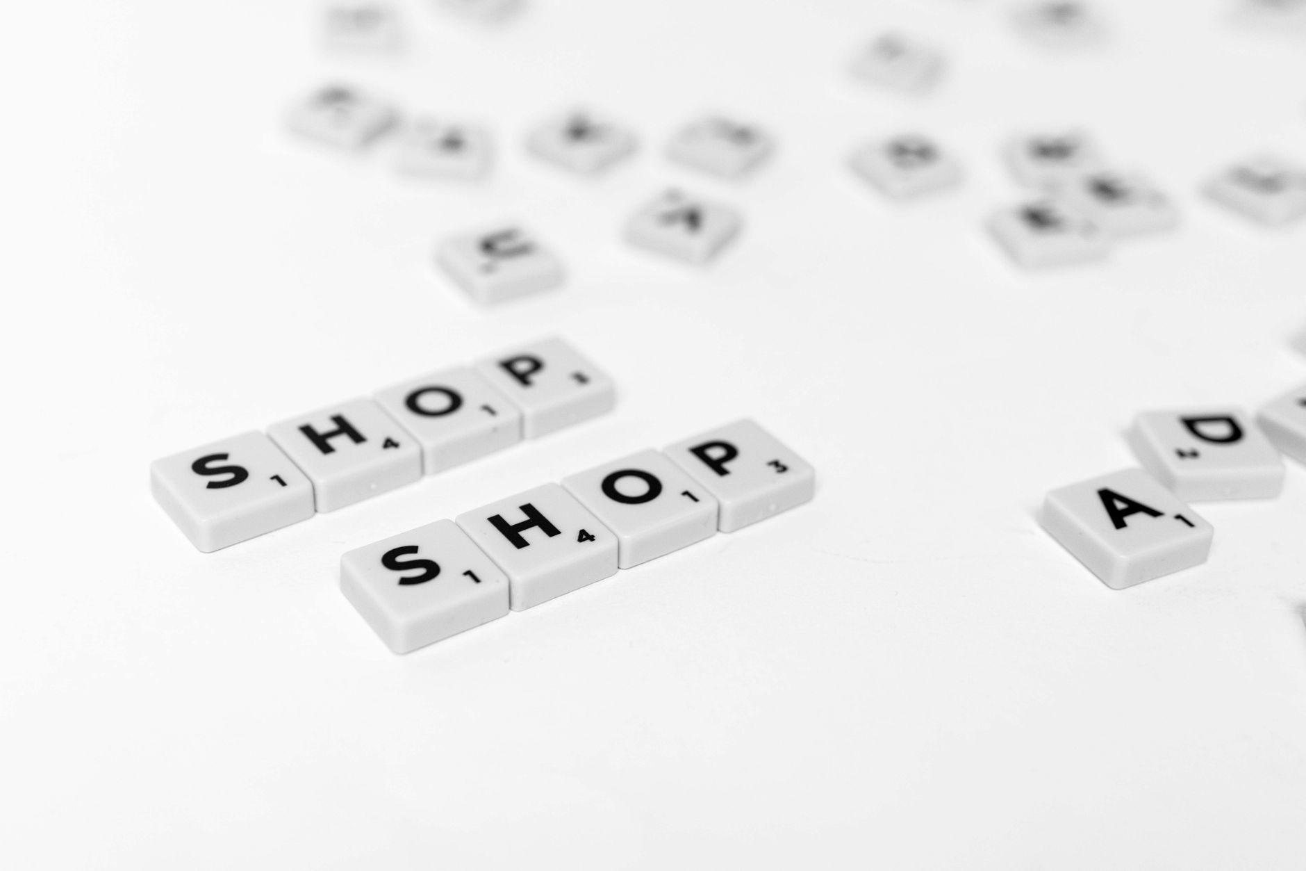 Gros plan sur des tuiles de lettres éparpillées épellent 'SHOP' sur un fond blanc propre.