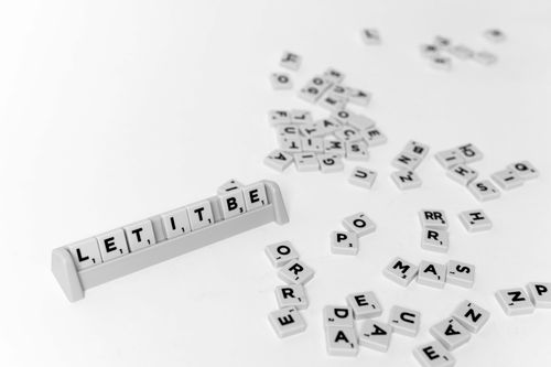 Free Scattered Scrabble tiles on a white background, forming the phrase 'Let It Be'. Stock Photo