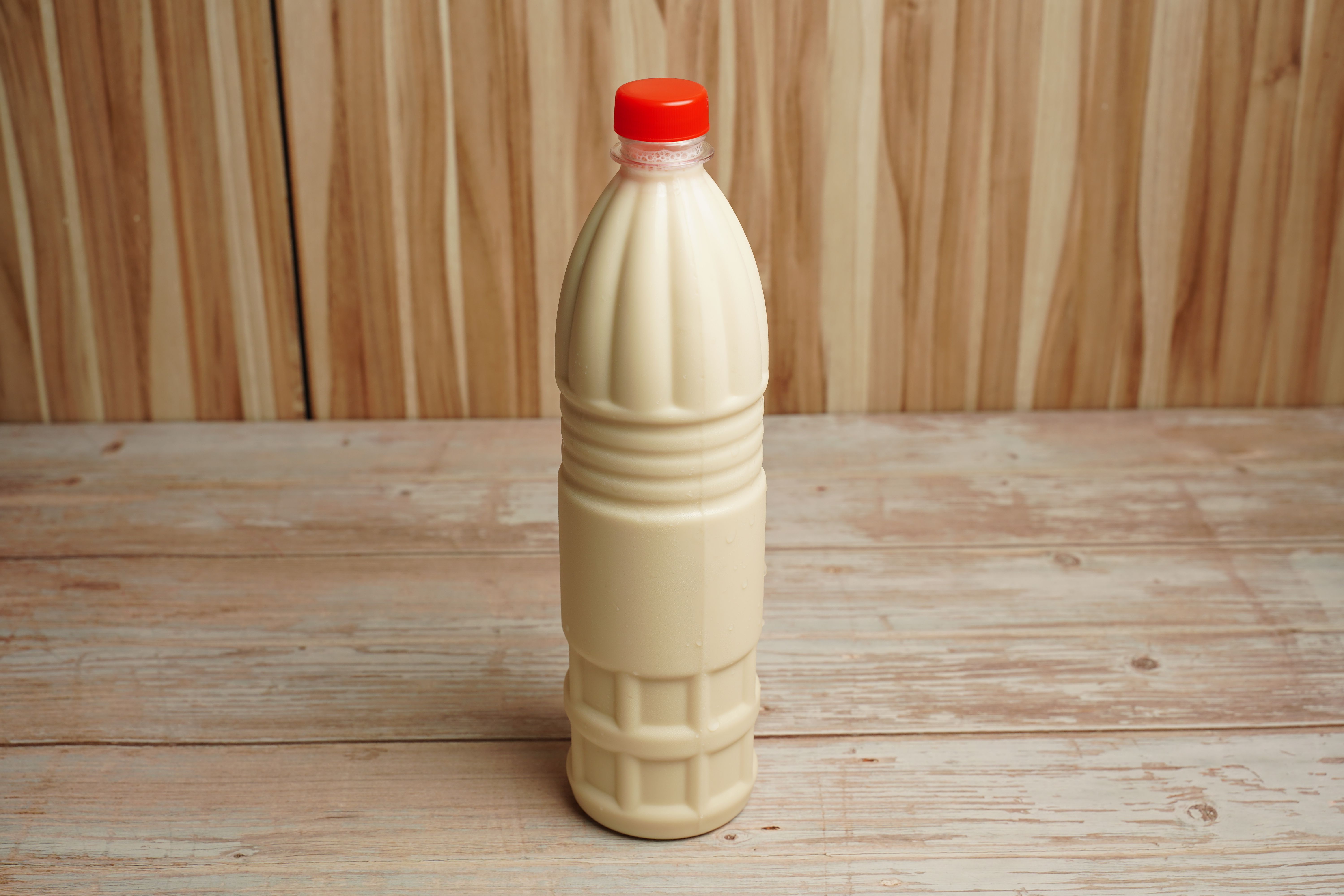 Close-up of a plastic milk bottle with a red cap on a rustic wooden table with copy space.