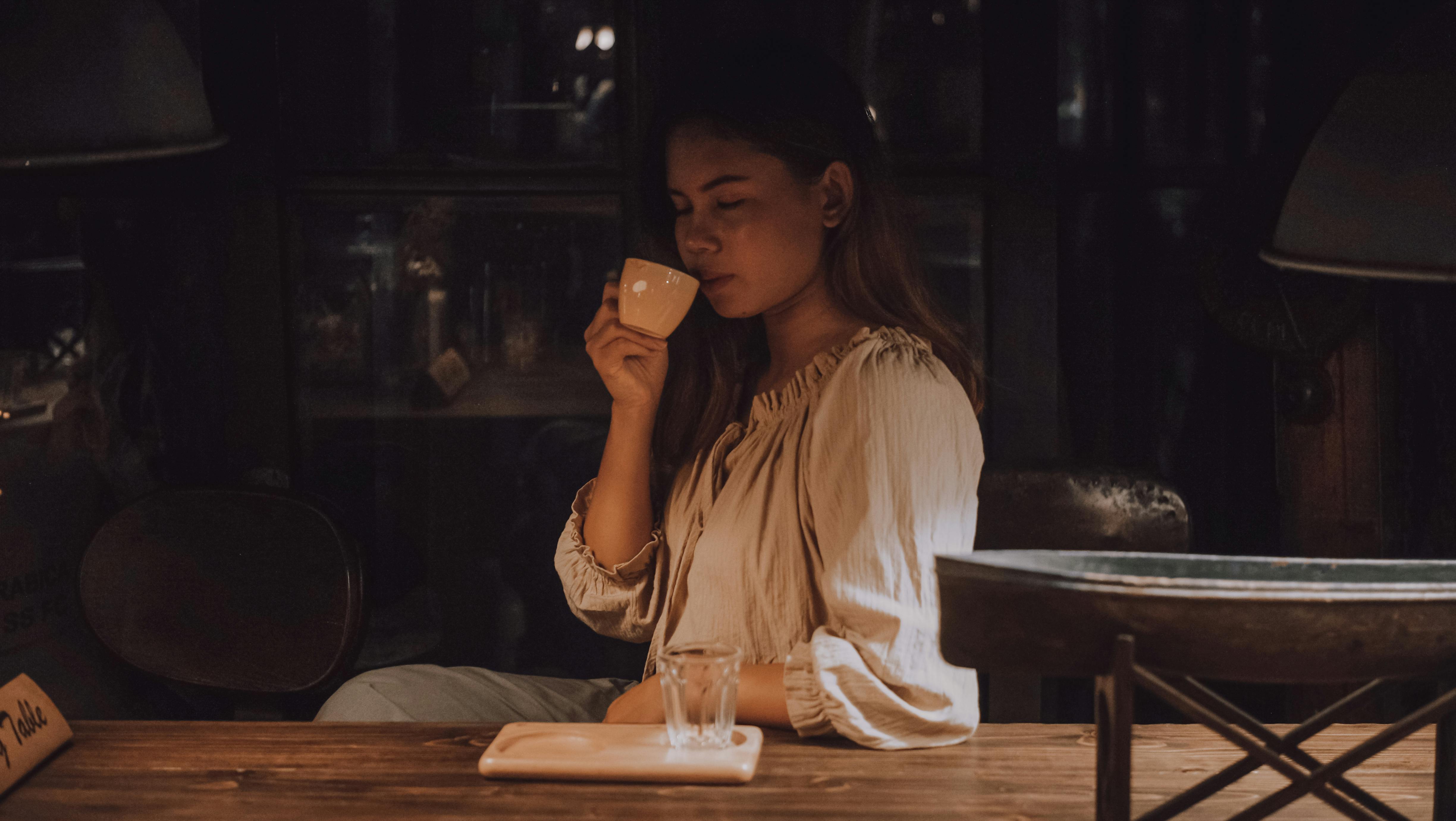 Woman enjoying a warm drink in a dimly lit cafe setting, creating a cozy and serene atmosphere.