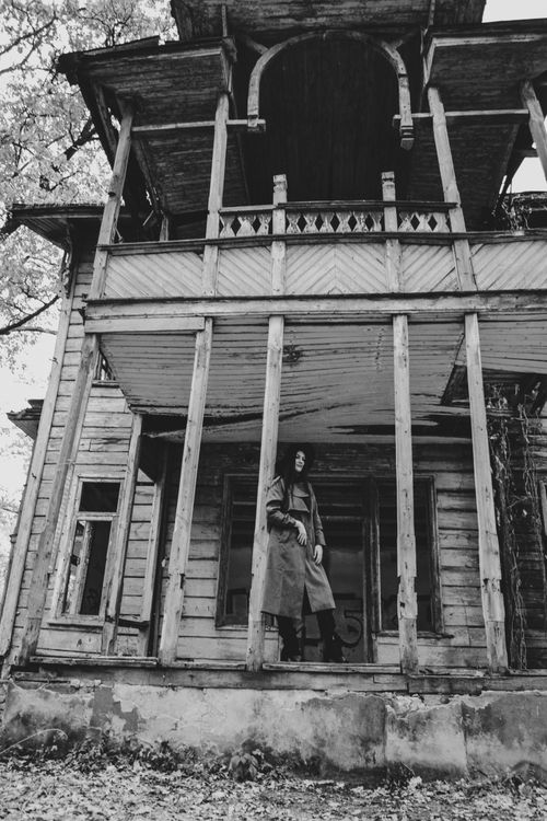 Free A solitary woman stands on the porch of an abandoned, dilapidated house in black and white. Stock Photo