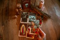 From above of crop unrecognizable tattooed female soothsayer showing tarot card with image above table with decorative bottles and amulet