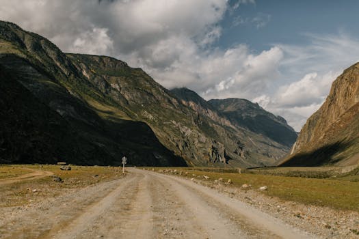 Explore a stunning mountain landscape with a dirt road meandering through rugged terrain under a dramatic sky.