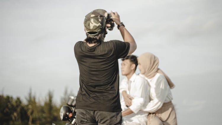 Back View Of A Photographer Taking Picture Of A Man And Woman Riding A Motorcycle