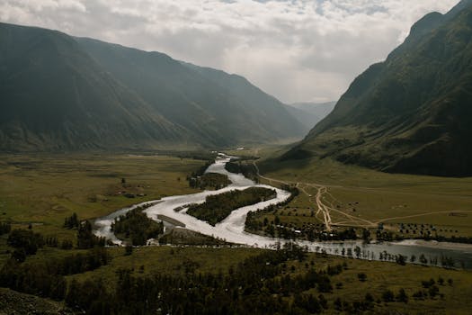 A breathtaking aerial photograph showcasing a winding river through a lush valley surrounded by majestic mountains.