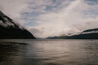 A serene lake view framed by majestic mountains under a cloudy sky, perfect for nature enthusiasts.