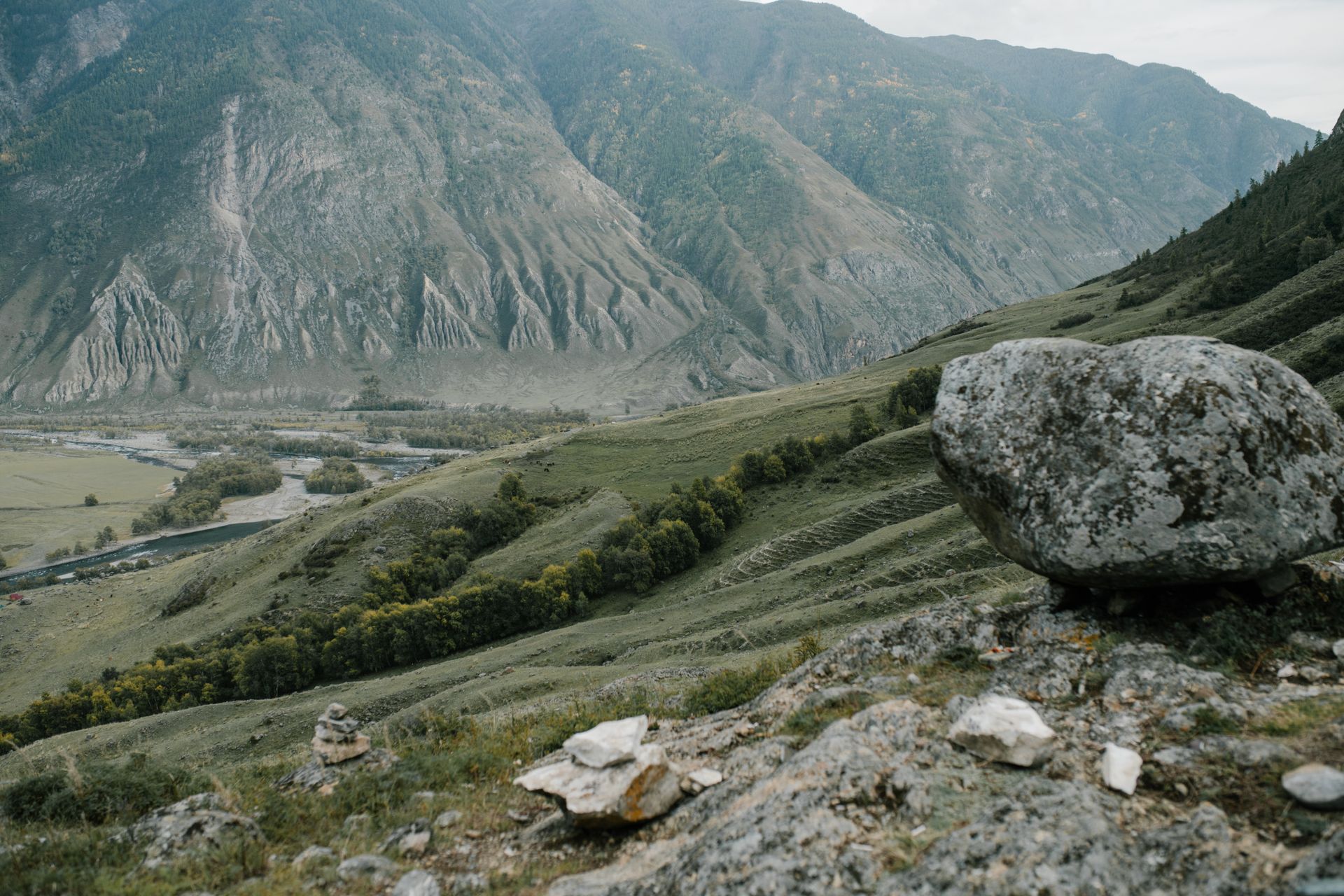 Breathtaking mountain landscape with a river valley and prominent rock formations under a soft light.