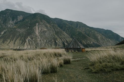 Free A wooden hut in a serene mountainous rural landscape under cloudy skies. Stock Photo