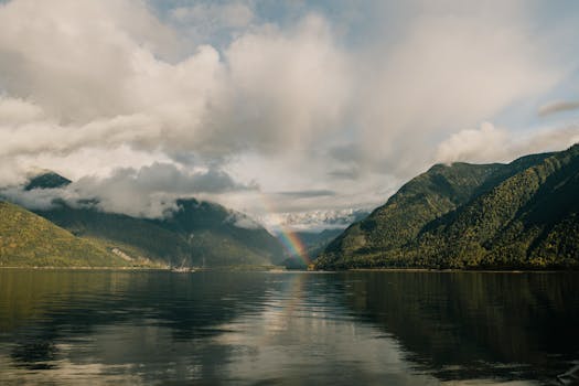 Peaceful mountain lake landscape with a vibrant rainbow and lush green hills.