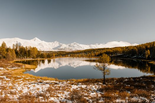 湖面宁静，倒映着秋日白雪皑皑的山脉与周围的森林