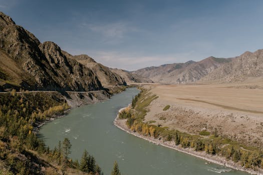 A scenic river winding through a majestic mountain landscape under a clear sky.