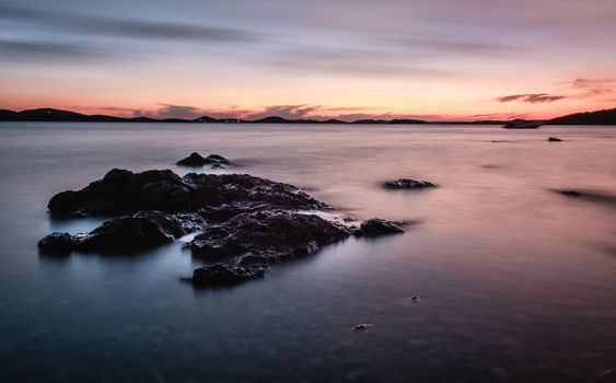 A tranquil seascape at sunset with rocks and calm waters, perfect for relaxation themes.