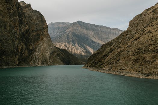 A tranquil lake nestled between towering rocky mountains under a cloudy sky, offering a sense of peace and isolation.