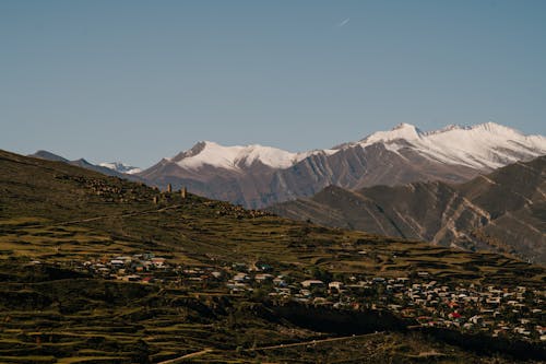 View of a Town on a Hill and Snowcapped Mountains under Blue Sky 