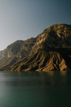 Breathtaking view of a towering mountain against a clear sky, reflecting on serene waters.