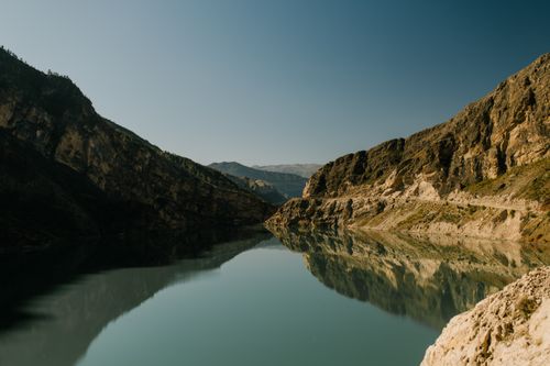 Free Serene mountain lake reflecting rocky cliffs under a clear blue sky. Stock Photo