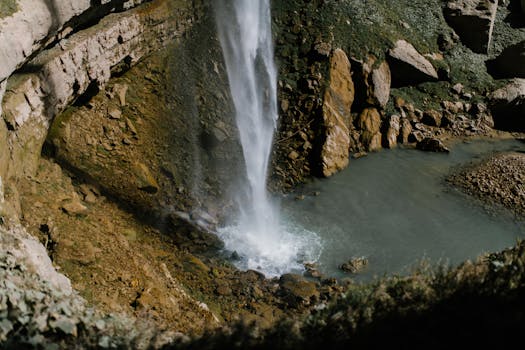 A breathtaking waterfall cascading down a rocky cliff into a serene pool surrounded by mossy rocks.