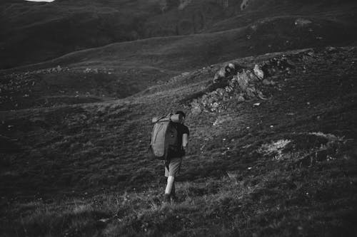 Grayscale Photo of Man Walking while Carrying a Backpack