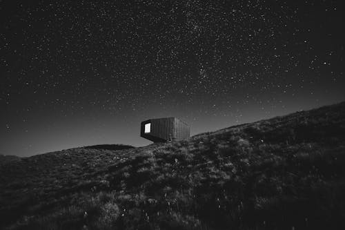 Grayscale Photo of House on Hill Under a Starry Night
