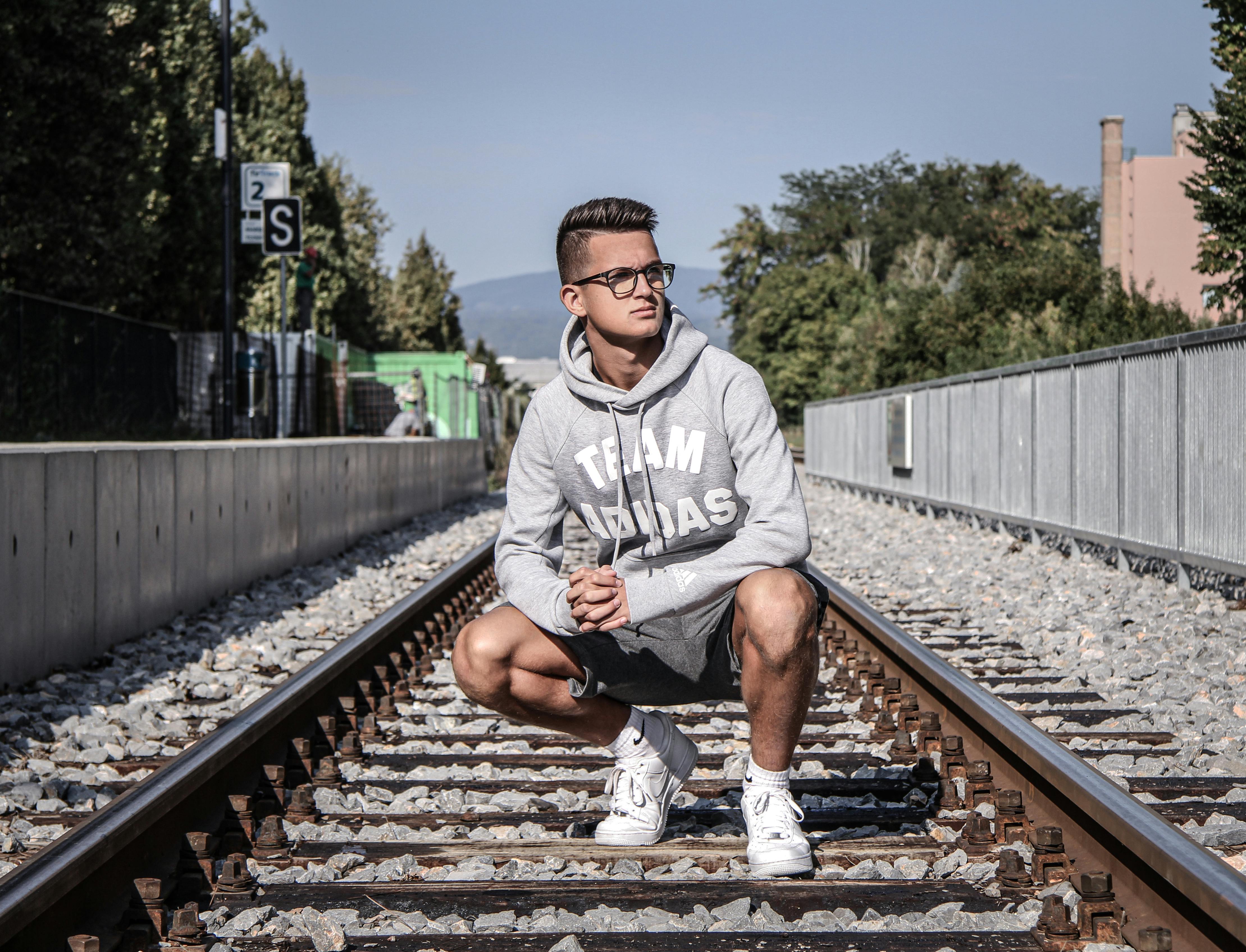 man in white and black adidas hoodie sitting on train rail