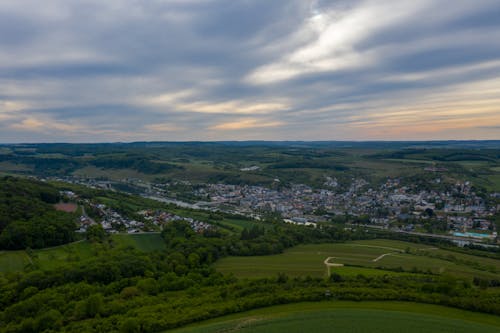 Aerial view of green fields and forest with small settlement located on river coast in cloudy day