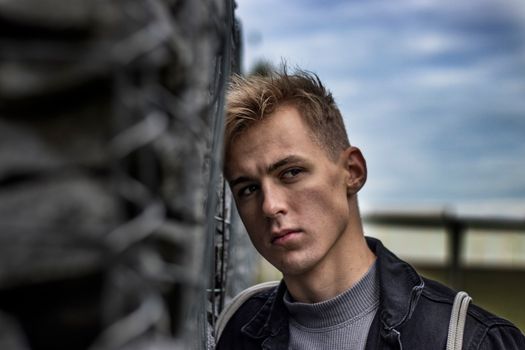 Close-up portrait of a serious young man leaning against a wire fence.