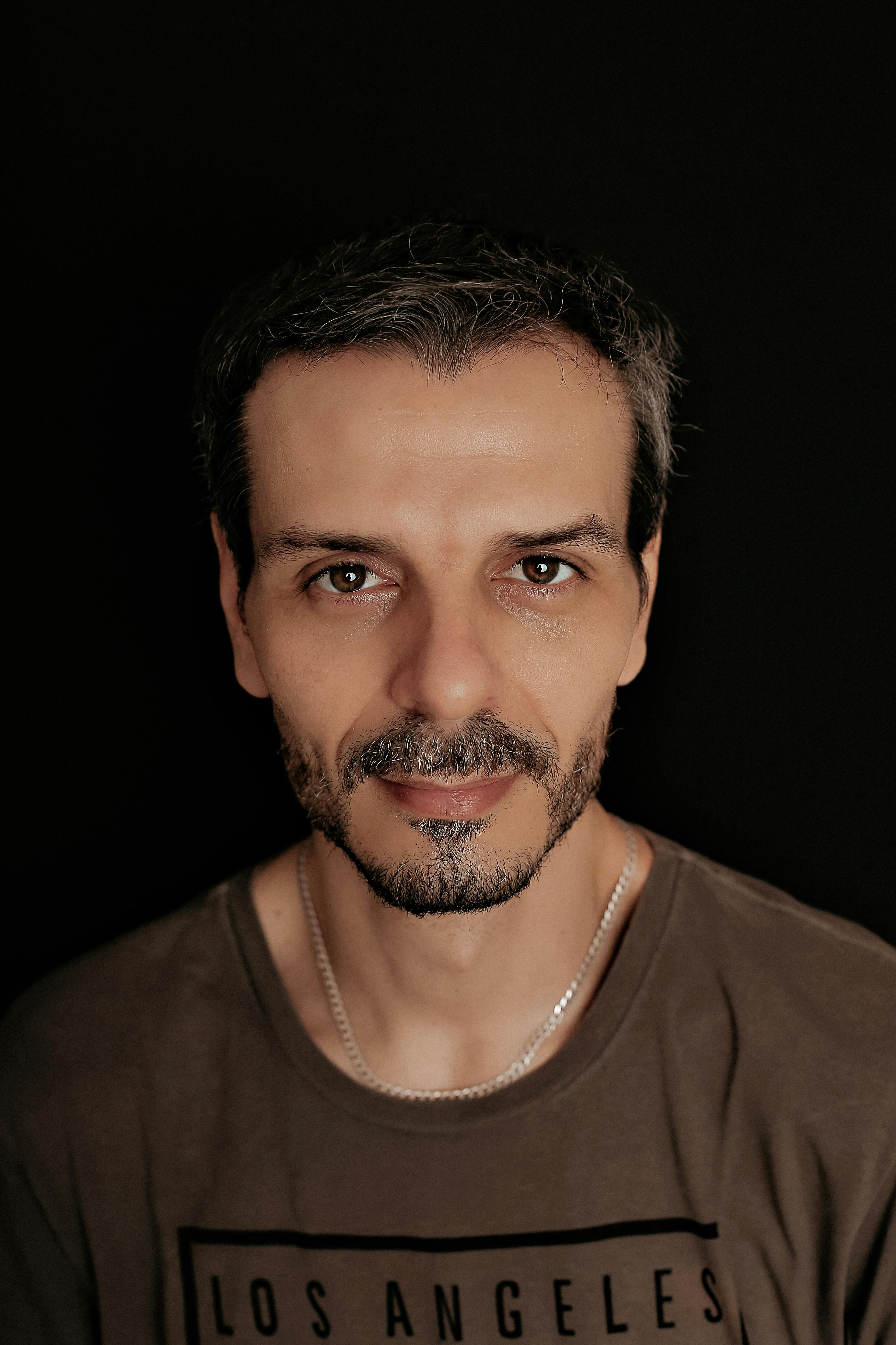 Close-up portrait of a bearded man wearing a brown shirt with a black background.