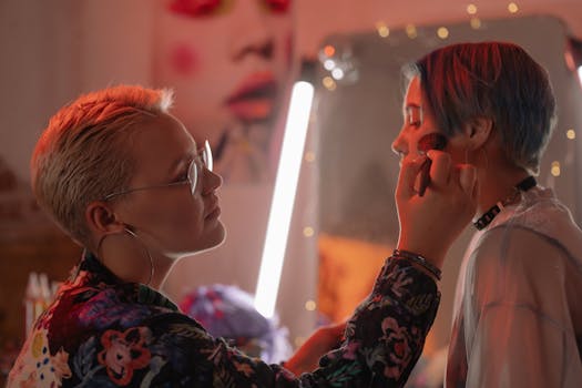 A makeup artist applying cosmetics to a woman in a warmly lit studio, creating a vibrant look.