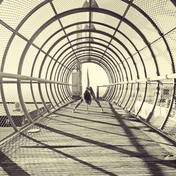 Monochrome female dancer bending forward in movement standing in round chain link overpass footbridge
