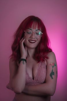 A confident woman with red hair and tattoos smiles in a playful studio portrait.