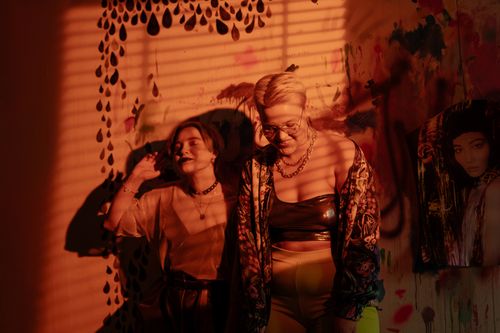 Free Two women in a stylish setting with graffiti, enjoying a playful moment in warm lighting. Stock Photo