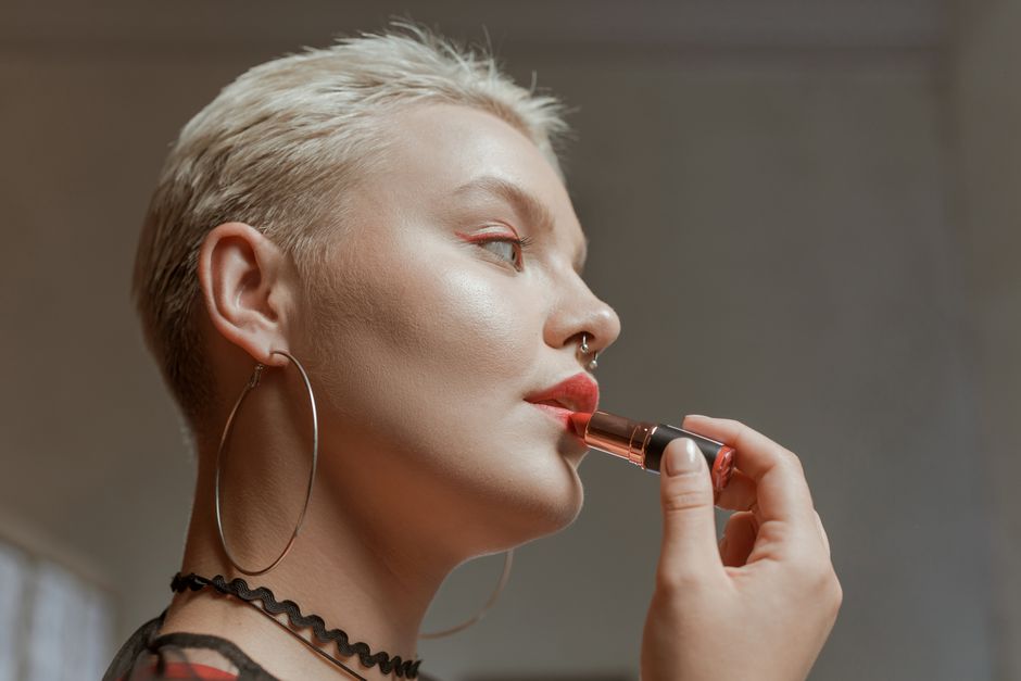 Close-up of a woman applying lipstick, showcasing her chic style with hoop earrings and a choker.
