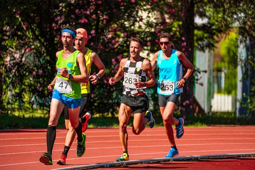 Group of young focused sportsmen in bright active wear running during track and field competition