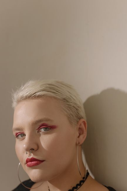 Striking portrait of a woman with short hair and bold red makeup, set in soft lighting.