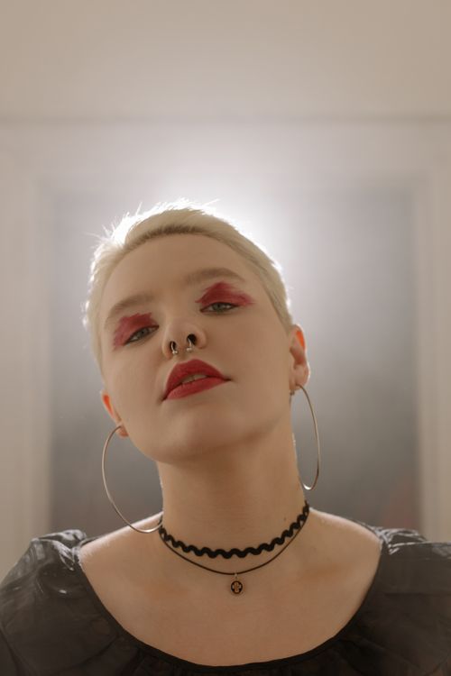 Free Close-up portrait of a woman with bold makeup, hoop earrings, and a choker, exuding a strong and confident vibe. Stock Photo