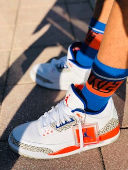 Close-up of stylish white sneakers with red accents worn outdoors on sunny day.