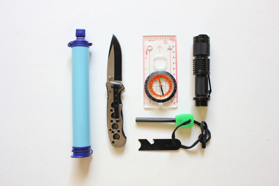 Flat lay of trail kit — water filter, knife, compass and torch on a white surface — Roger Brown on Pexels