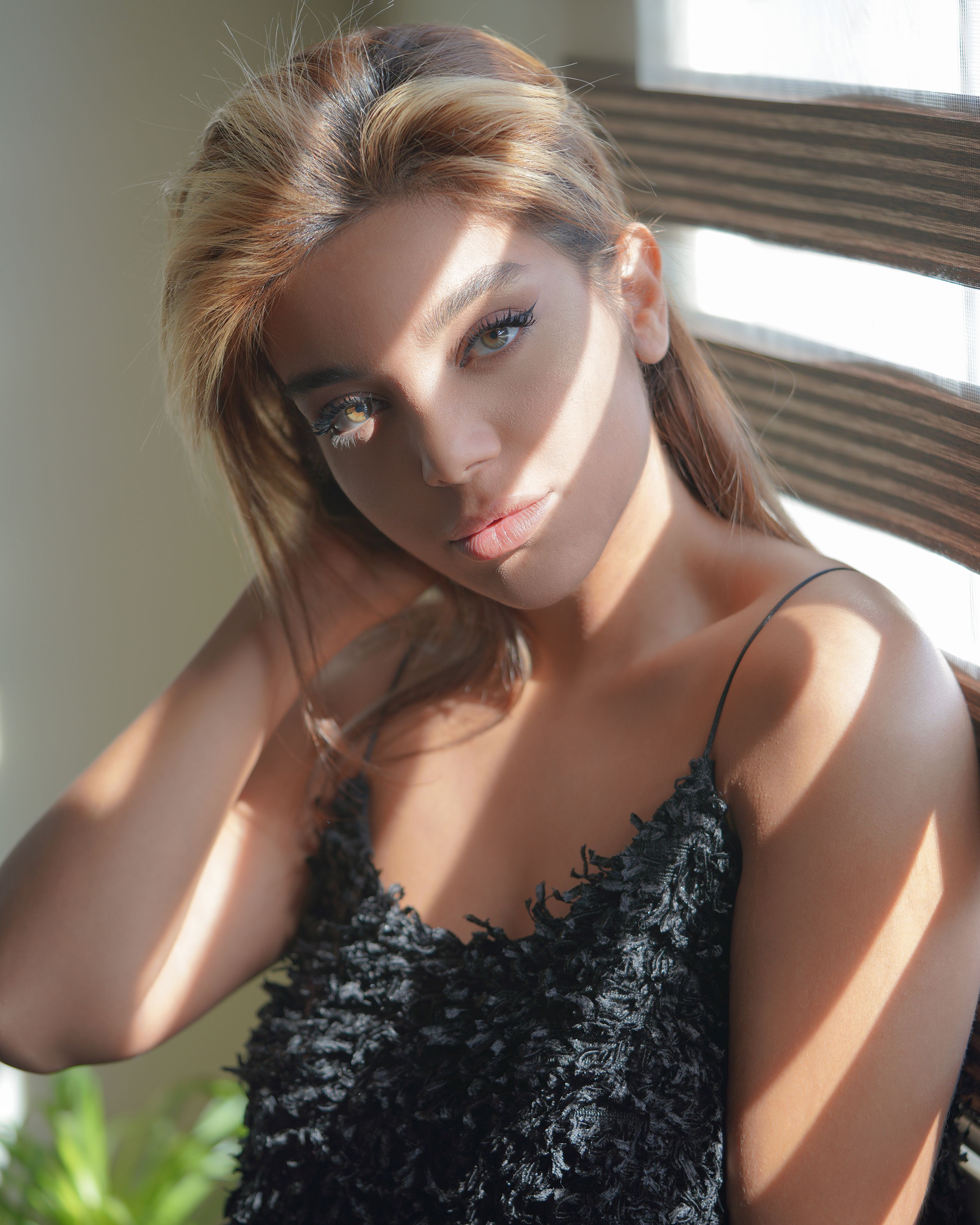 Portrait of a stylish woman indoors with sunlight casting shadows across her face.