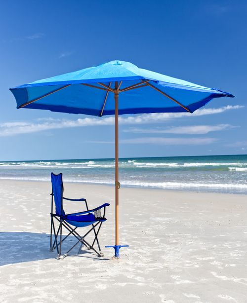 Free Serene beach scene with a blue umbrella and chair under a bright sky. Stock Photo