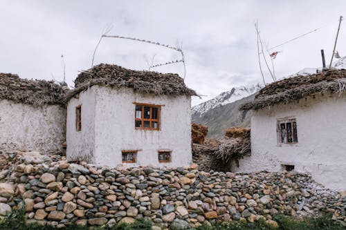 Exterior of grunge white stone shacks with thatch roof surrounded with stone fence and located on rough rocky mountain bottom