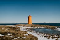 冰岛岩石海岸上的橙色灯塔，蓝蓝的天空和遥远的山脉