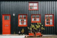 Front view of a traditional Icelandic black house with red doors and windows, plants in front.
