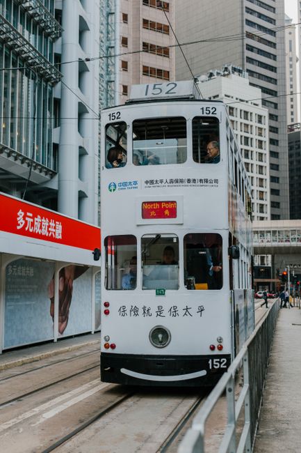 Double-decker tram in Hong Kong city center amidst skyscrapers, vibrant urban life.