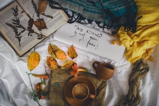 From above arrangement of cups placed near opened book and colorful scarfs with envelope on white sheet with autumnal leaves