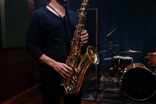 Close-up of a saxophone player in a dimly lit music studio with drums in the background.