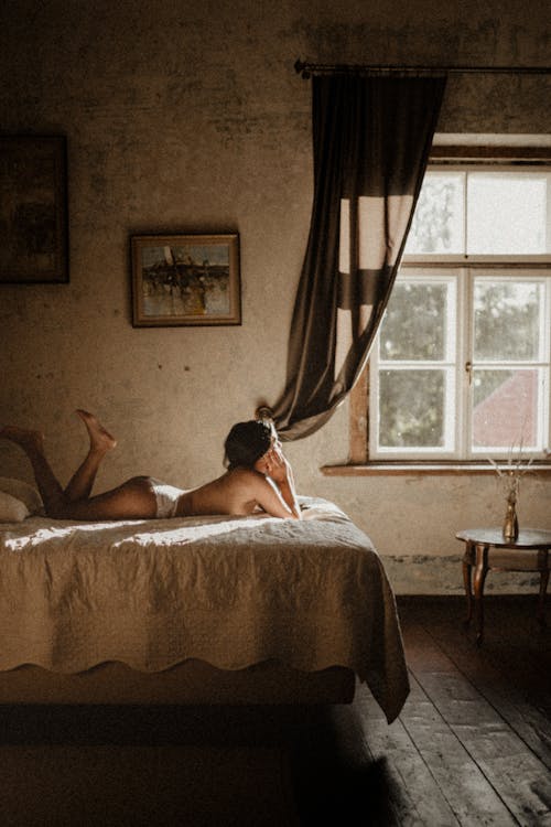Free Side view unrecognizable slim female in white panties resting on comfortable bed in light bedroom with old fashioned interior items Stock Photo