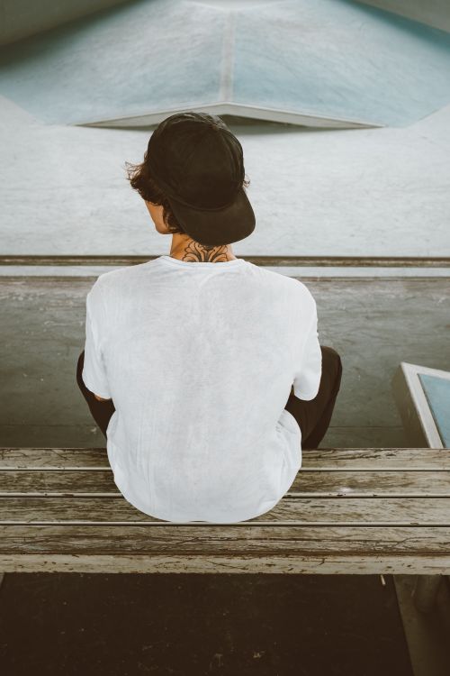 Free Back view of a boy wearing a baseball cap sitting on a bench at a skatepark. Stock Photo