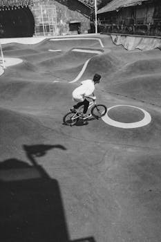Black and white image of a BMX rider in an outdoor skate park showcasing extreme sports action.